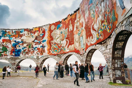 Visitors exploring the colorful David the Builder monument with traditional Georgian artistic murals and stone arches in Tbil